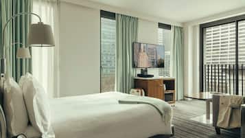 Ett hotellrum med en säng, ett skrivbord, en tv och utsikt över stadsbilden genom fönstret.