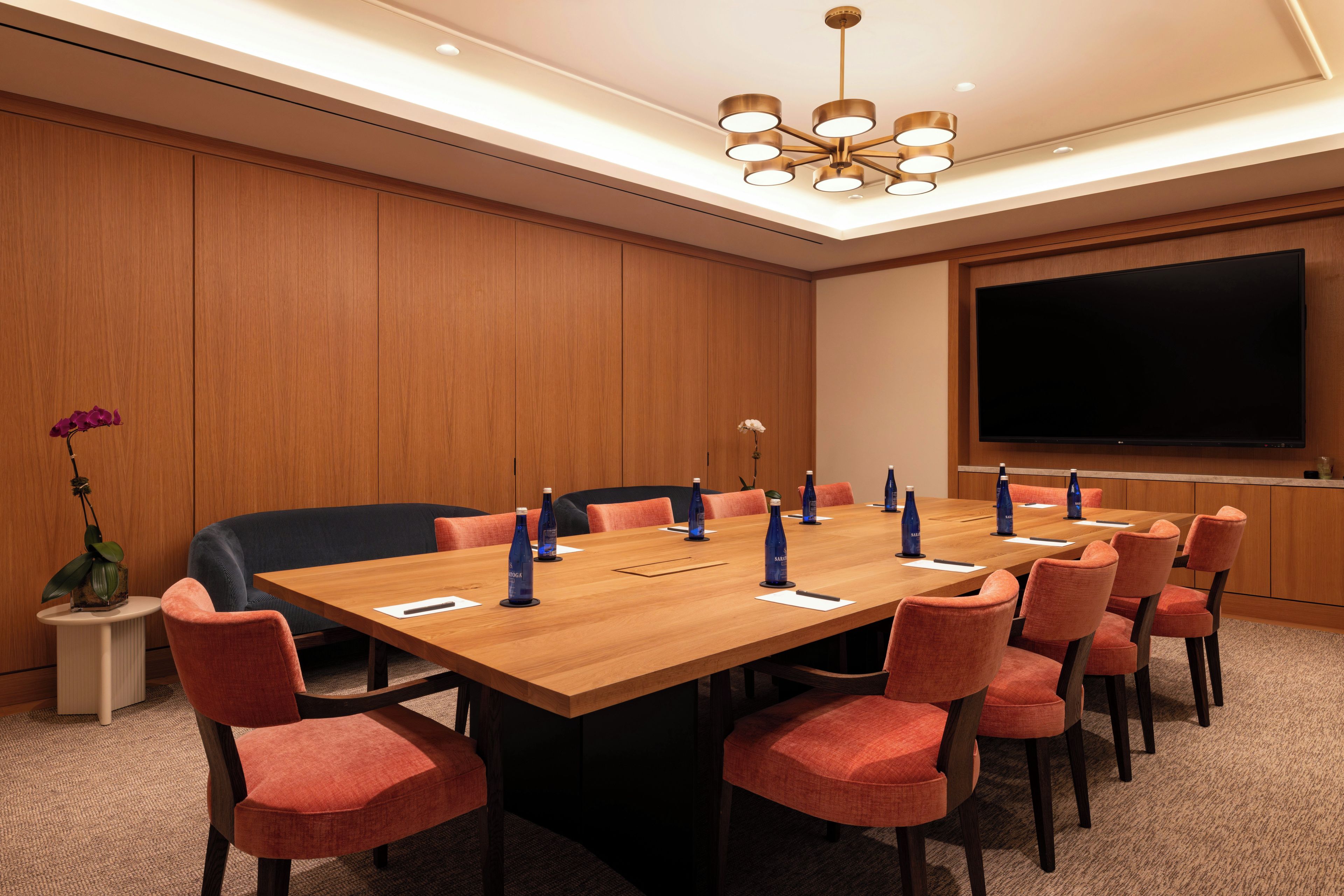 A conference room with a large wooden table, red upholstered chairs, and a large screen on the wall.