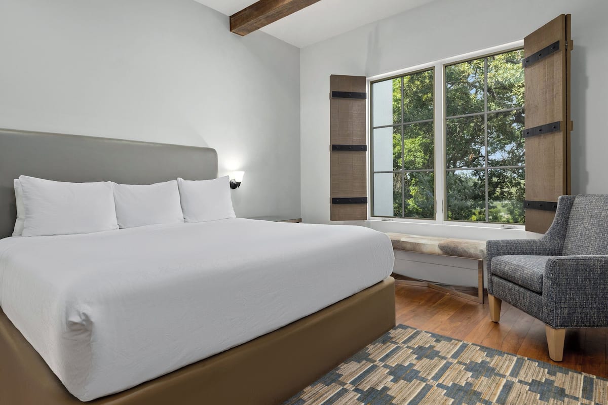 Een moderne slaapkamer met een groot bed, een raam met uitzicht op bomen en een stoel.