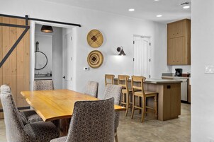 A modern kitchen with wooden cabinets, a central island, and a dining area with patterned chairs.