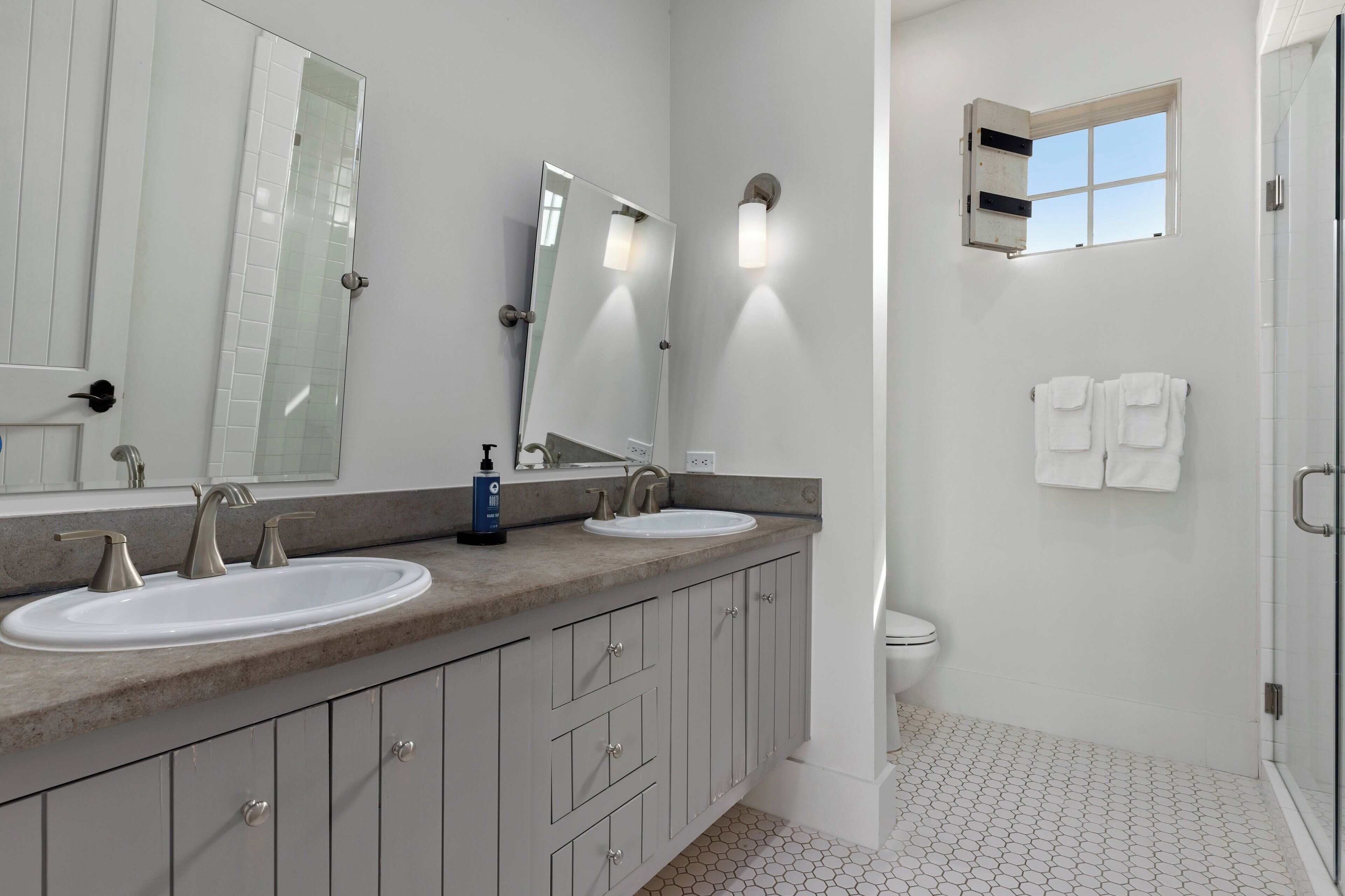 A modern bathroom with two sinks, a large mirror, and a shower area.