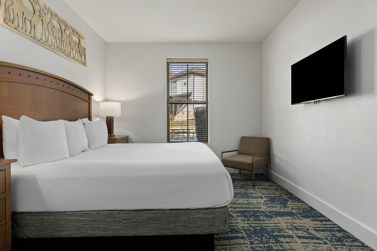 Hotelkamer met een groot bed, een flatscreen televisie aan de muur, een raam met zonwering en een kleine stoel.