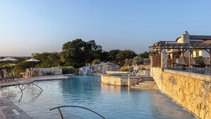 Une piscine avec des murs en pierre, des chaises longues et des parasols.