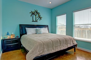 A bedroom with a bed, nightstand, and a wall decoration of palm trees.