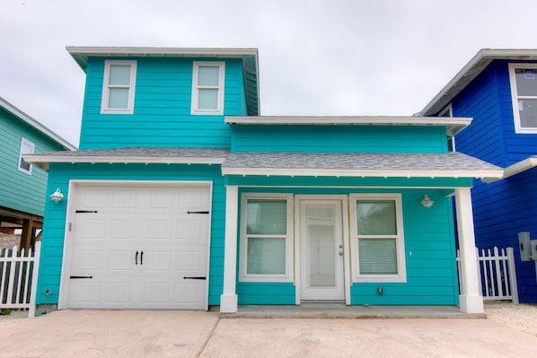 A two-story house with a white garage door, a front door with a glass panel, and a small porch area.