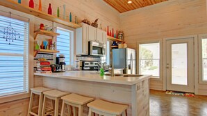A modern kitchen with white cabinets, a central island with stools, and a wooden ceiling. - 6 On The Beach VW6 (Port Aransas)
