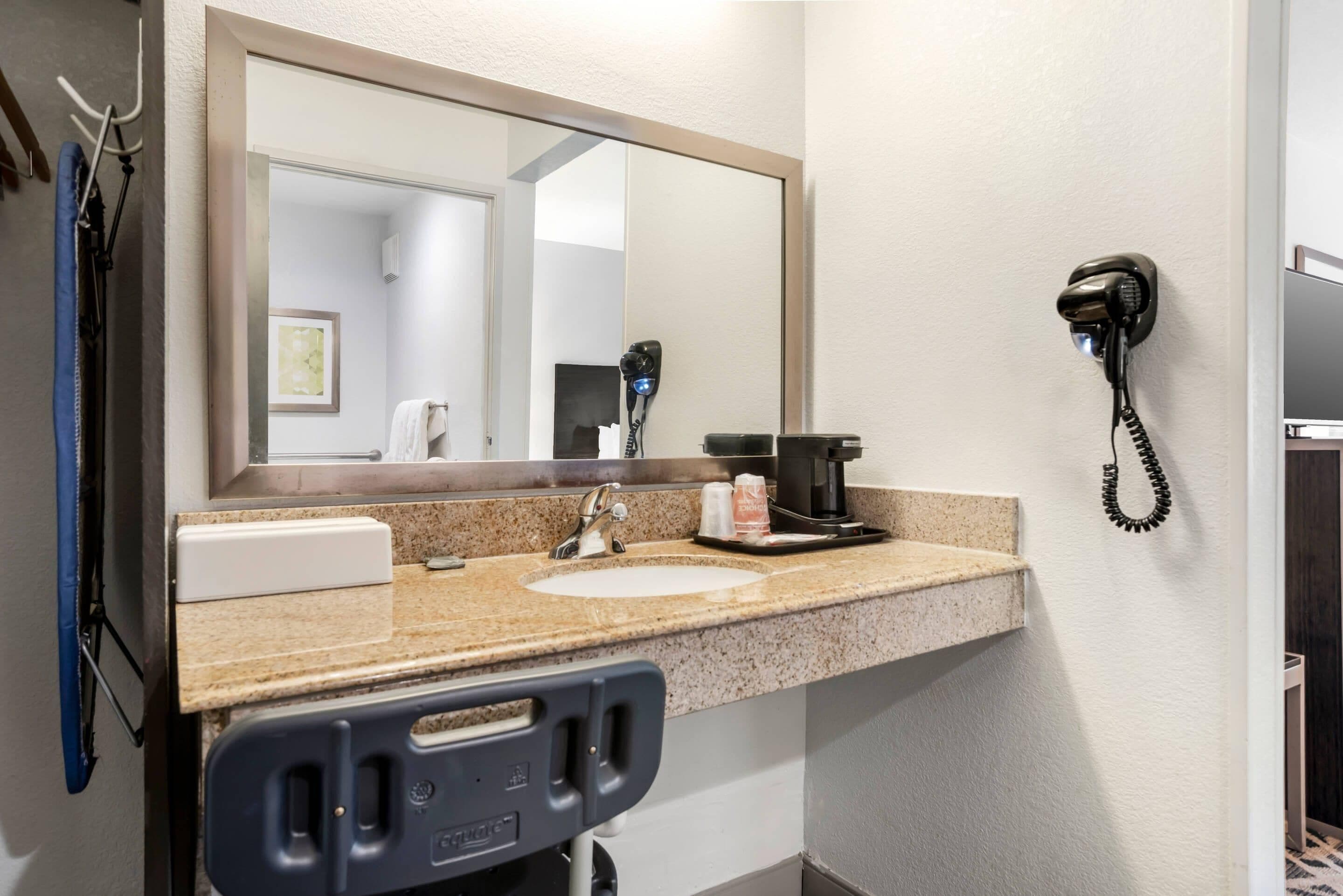 A bathroom with a sink, mirror, hair dryer, and a telephone.