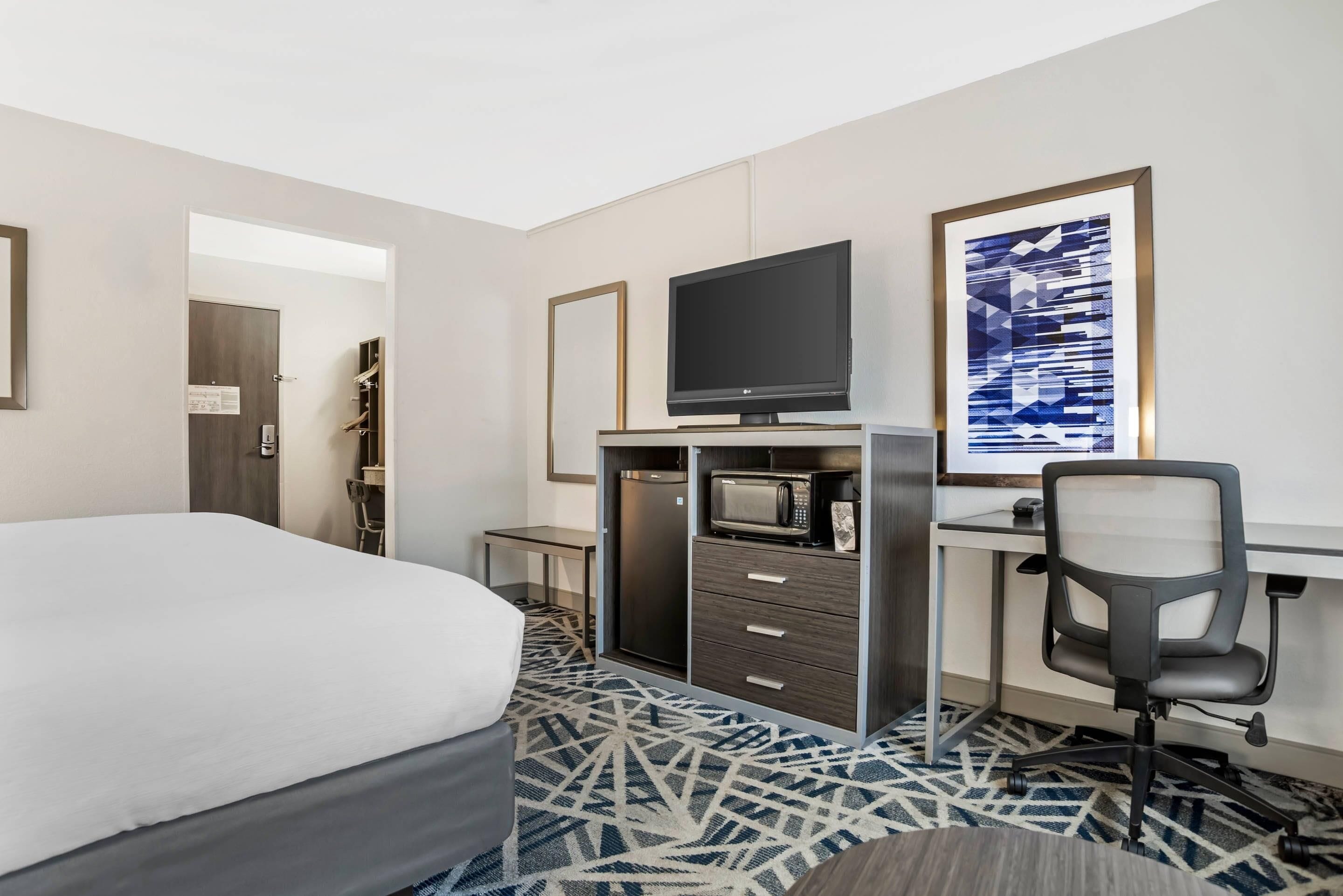 Une chambre d’hôtel équipée d’un lit, d’un bureau avec un ordinateur, d’une télévision, d’un four à micro-ondes et d’une chaise.