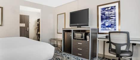 A hotel room with a bed, a desk with a computer, a TV, a microwave, and a chair.
