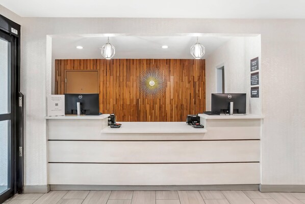 A reception desk with two computer monitors, a coffee machine, and a decorative wall panel. - Country Inn & Suites by Radisson, Montgomery East I-85 (Montgomery)