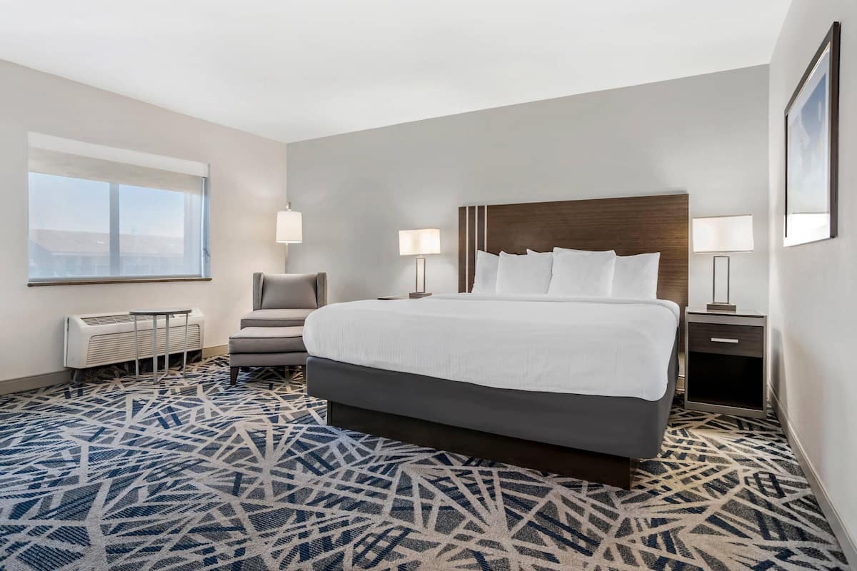 A hotel room with a large bed, two bedside tables, a chair, a window, and an air conditioning unit.