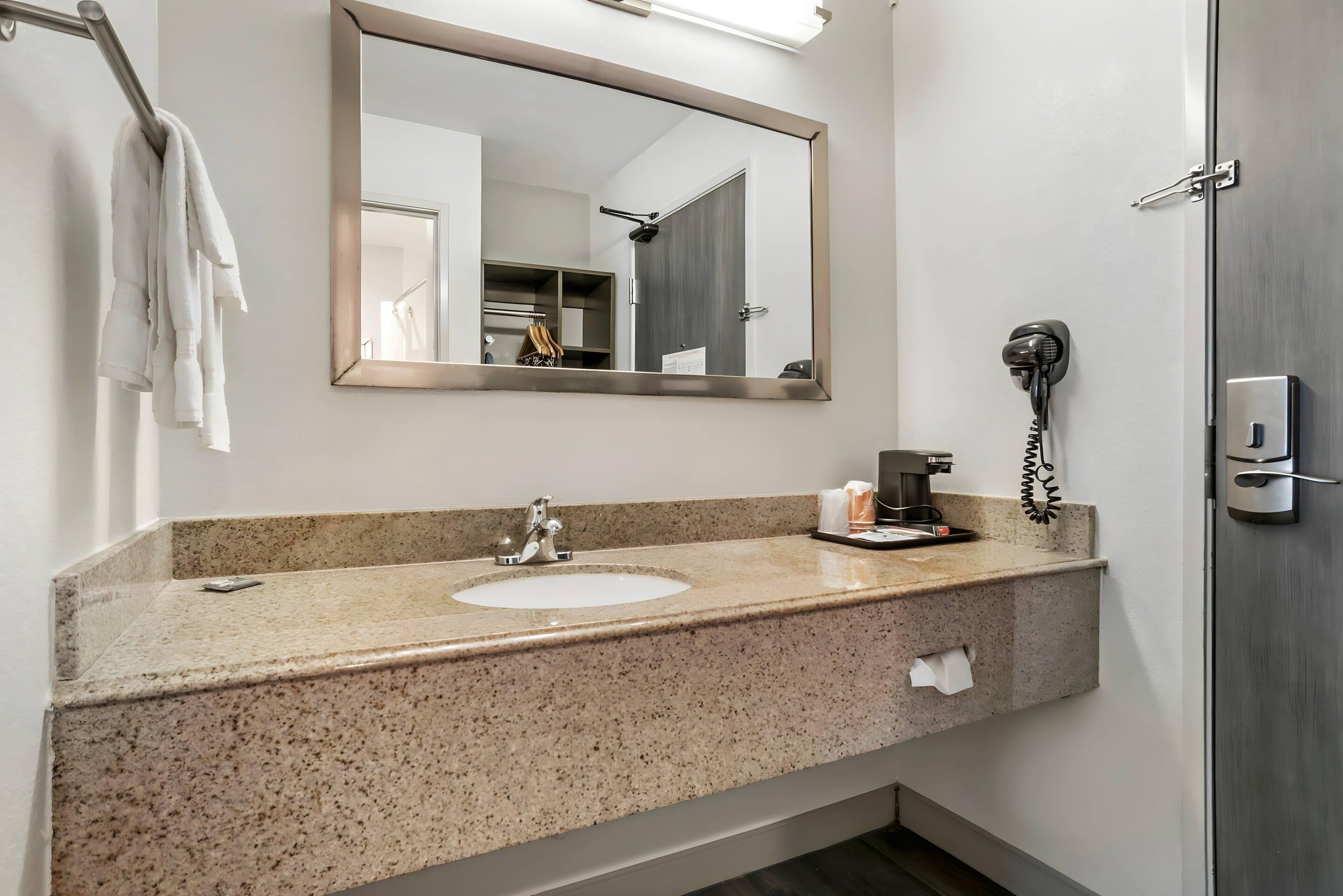A bathroom with a granite countertop sink, a mirror, a hairdryer, and a towel rack.