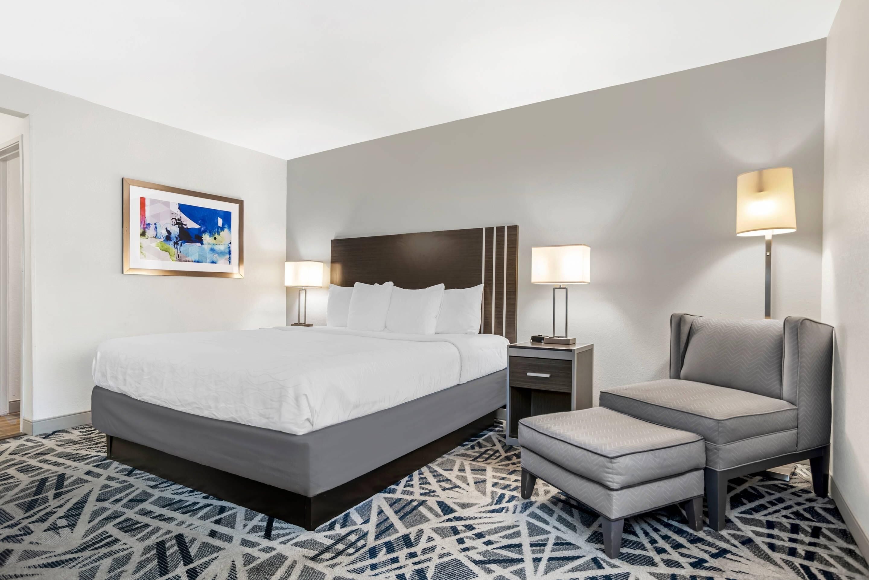 Une chambre d’hôtel avec un grand lit, des lampes de chevet, une chaise et un tapis à motifs.