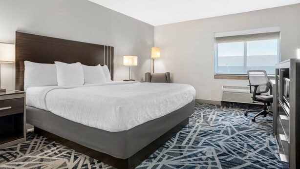 A hotel room with a large bed, bedside lamps, a desk, and a view of the outdoors.