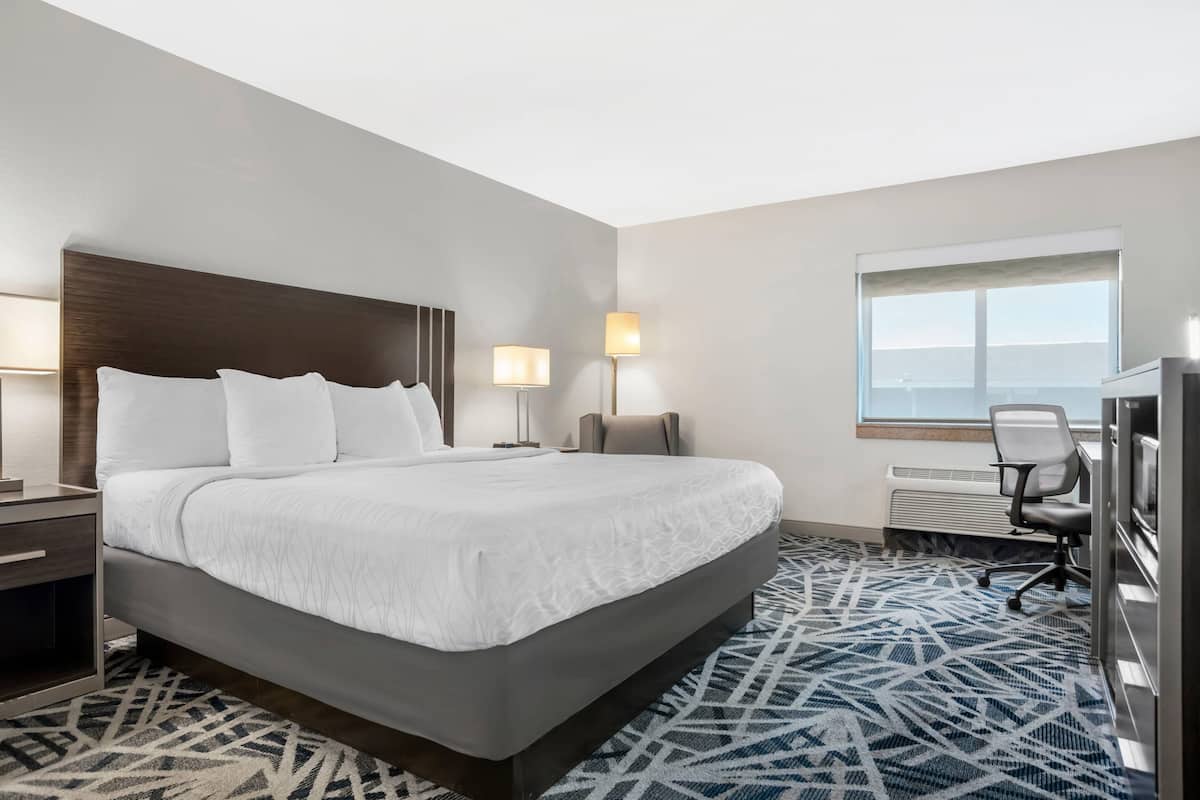 A hotel room with a large bed, bedside lamps, a desk, and a view of the outdoors.