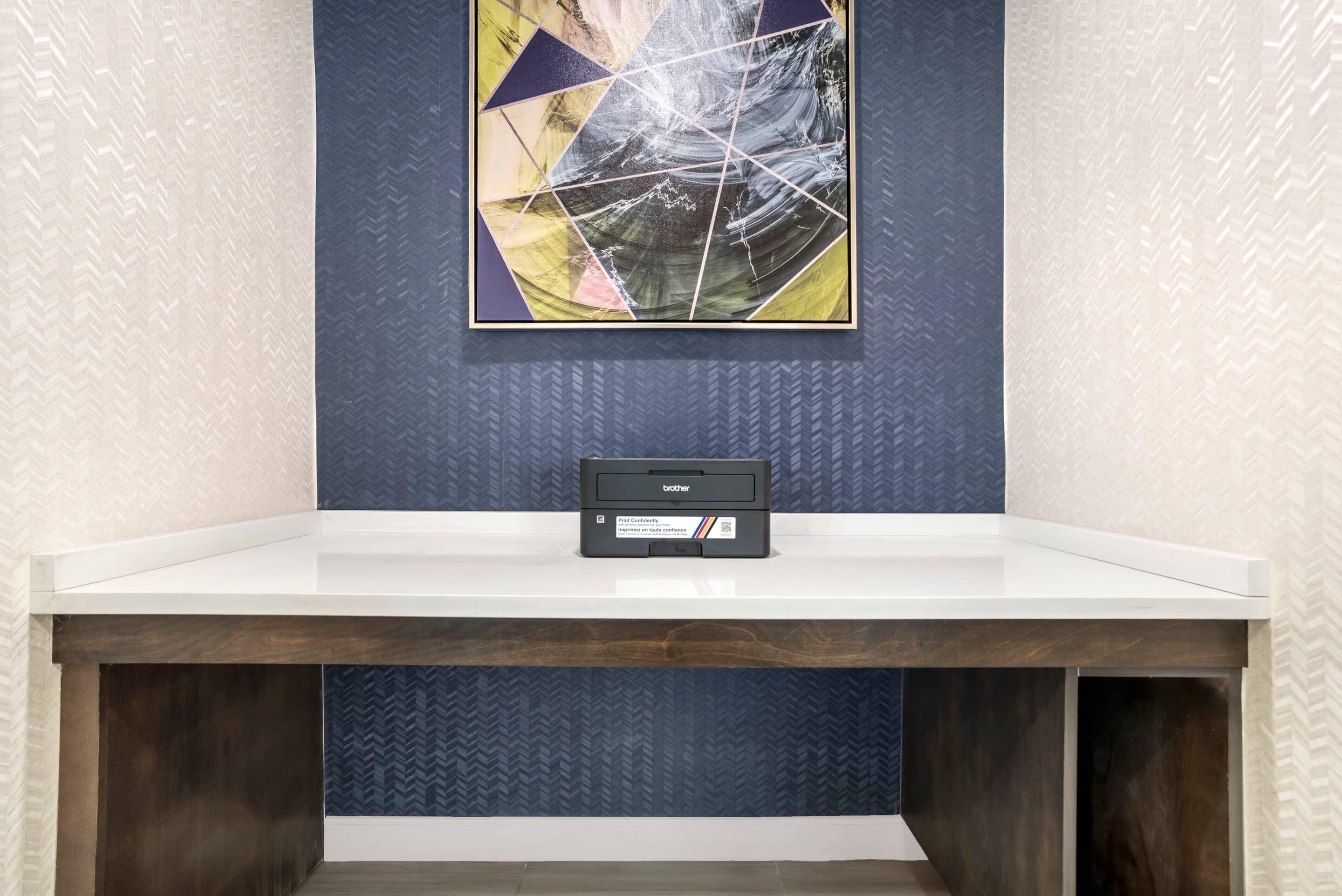 Een receptiebalie van een hotel met een modern design, met daarboven een ingelijst abstract schilderij en een Brother printer op de toonbank.