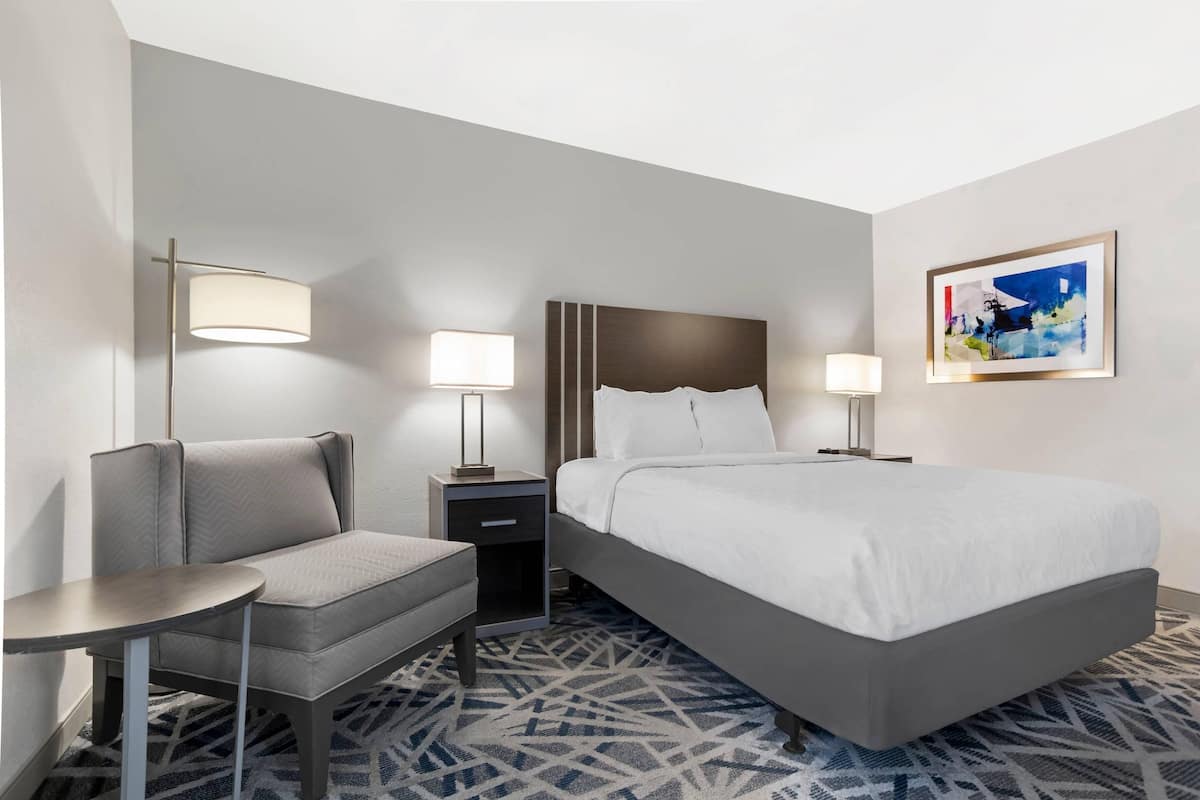 A hotel room with a bed, bedside tables, a chair, and a patterned carpet.