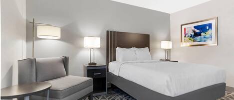 A hotel room with a bed, bedside tables, a chair, and a patterned carpet.