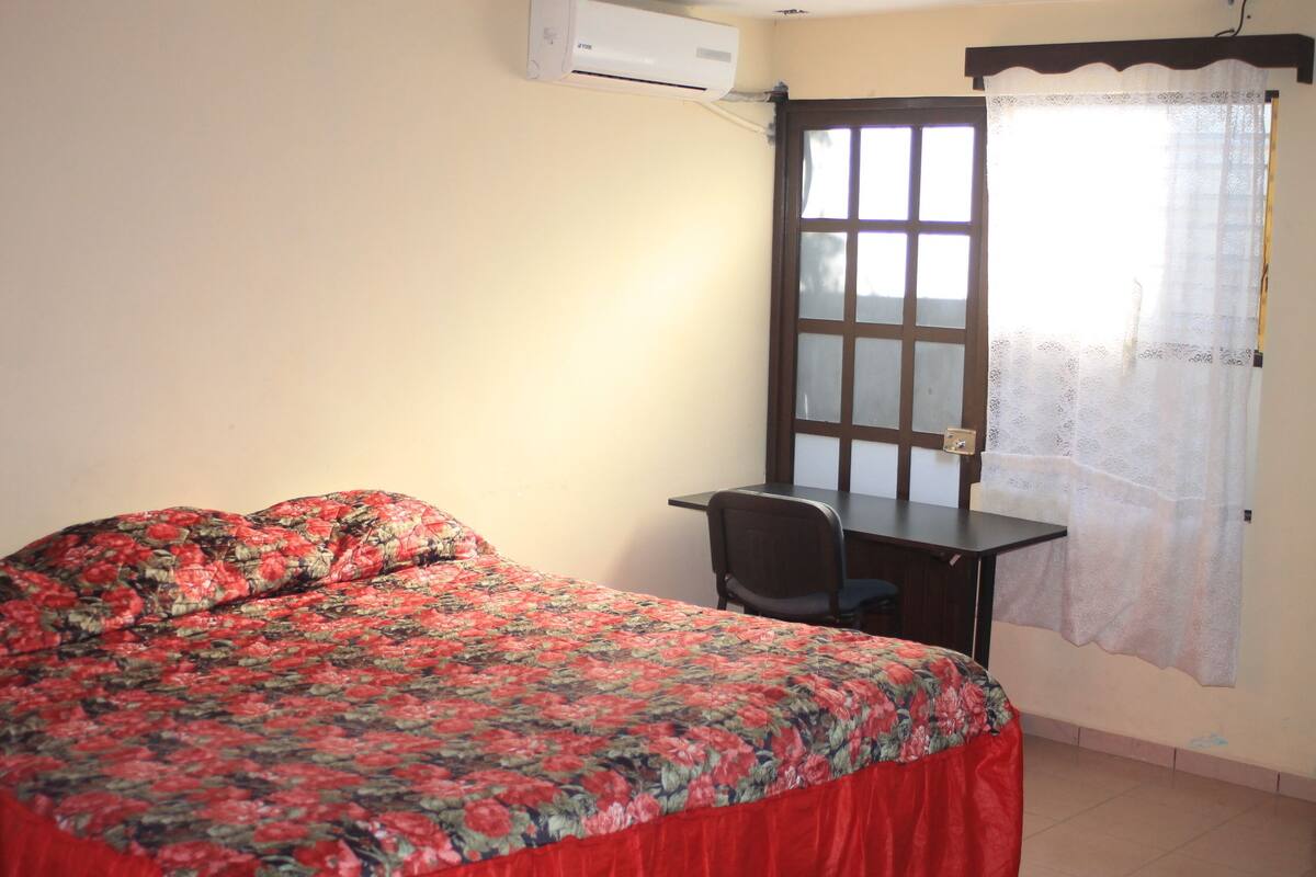 A room with a bed, a desk, and a window with a curtain.