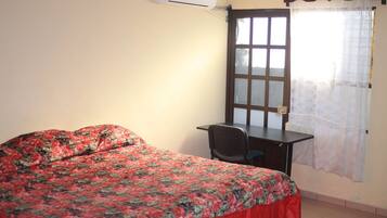 A room with a bed, a desk, and a window with a curtain.