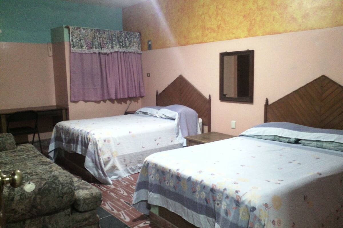 A room with two single beds, a small table, and a chair.