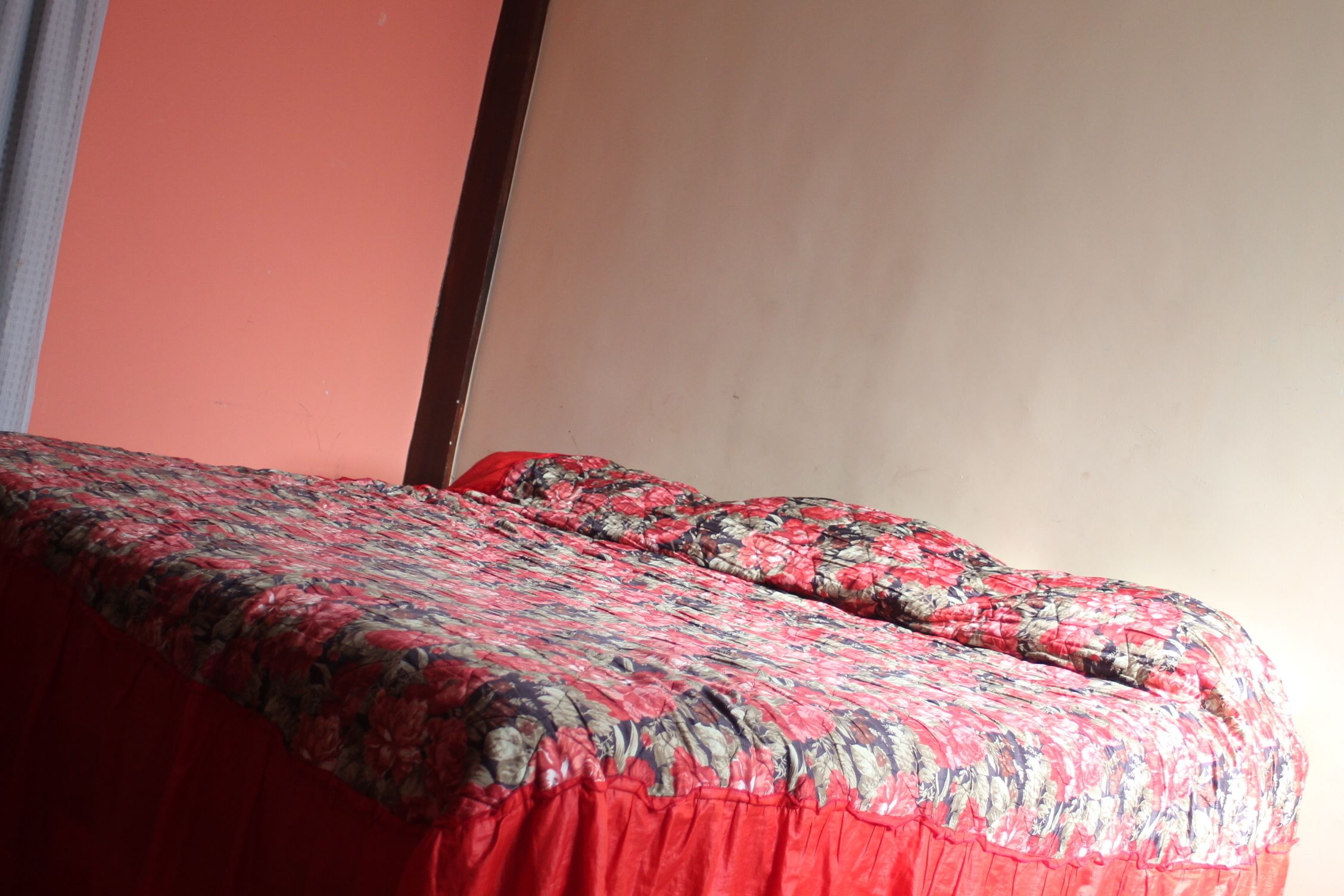 A bed with a floral-patterned bedspread and a red skirted duvet.