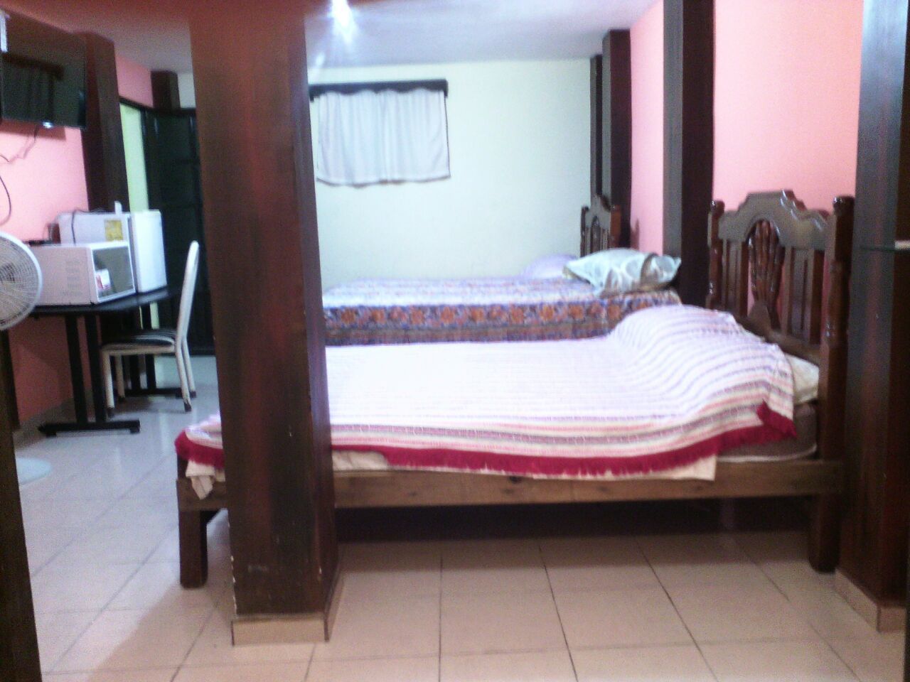 A bedroom with a bed, a desk with a chair, a fan, and a window with curtains.