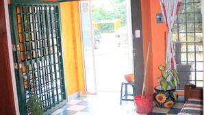 A room with a checkered floor, a green door with a metal grille, a window with a curtain, and a potted plant. - Hotel Acuarela Huasteca (Ciudad Valles)