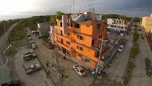 A multi-story hotel with a prominent orange facade, located at a street corner with visible parking and a Coca-Cola sign. - Hotel Acuarela Huasteca (Ciudad Valles)