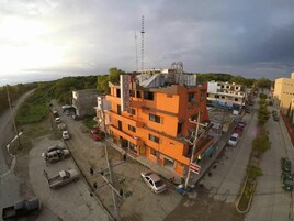 Un hotel de varios pisos con una fachada anaranjada destacada, situado en una esquina con estacionamiento visible y un letrero de Coca-Cola.