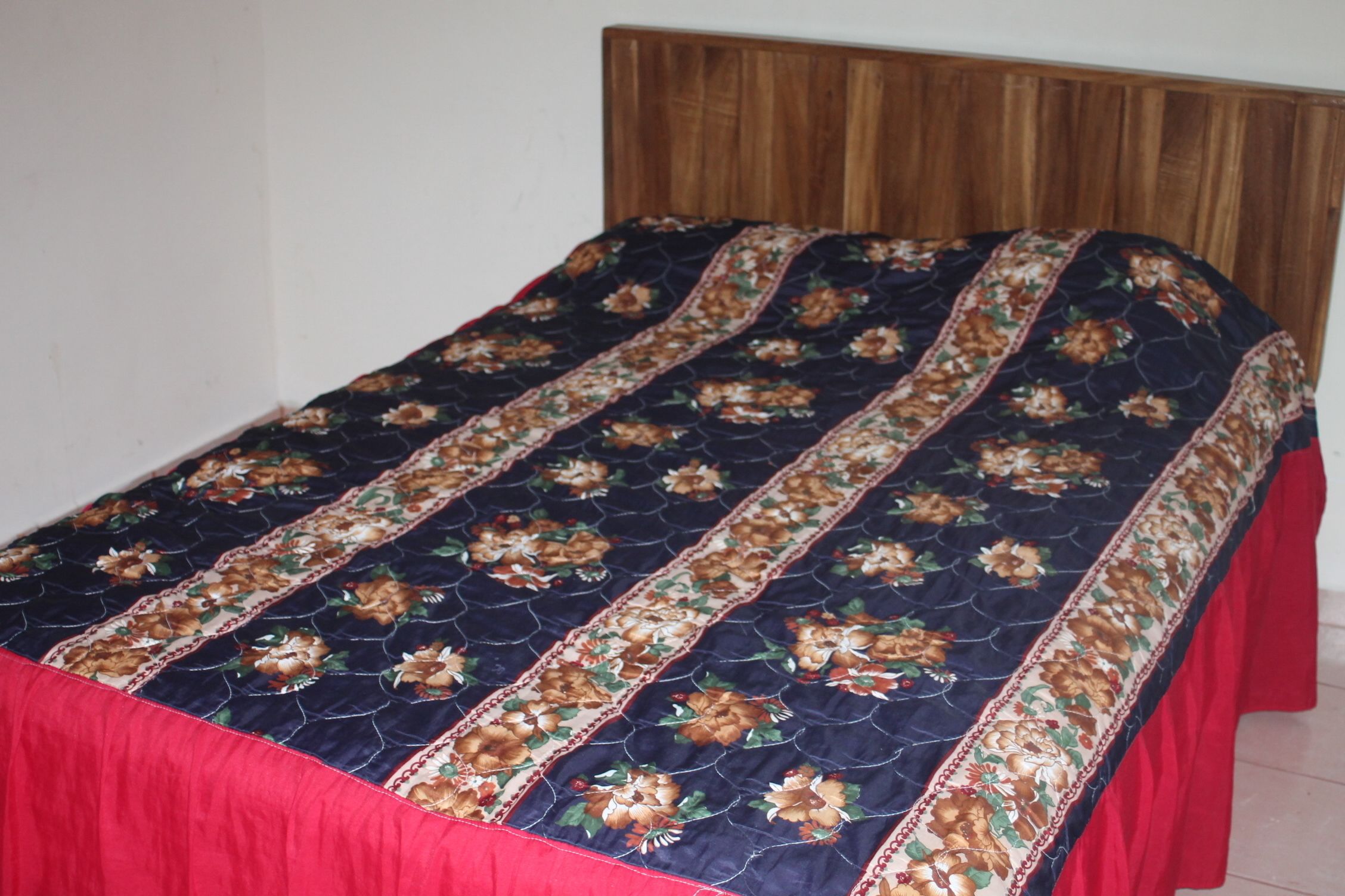 Una cama con una colcha estampada con motivos florales y cortinas rojas.