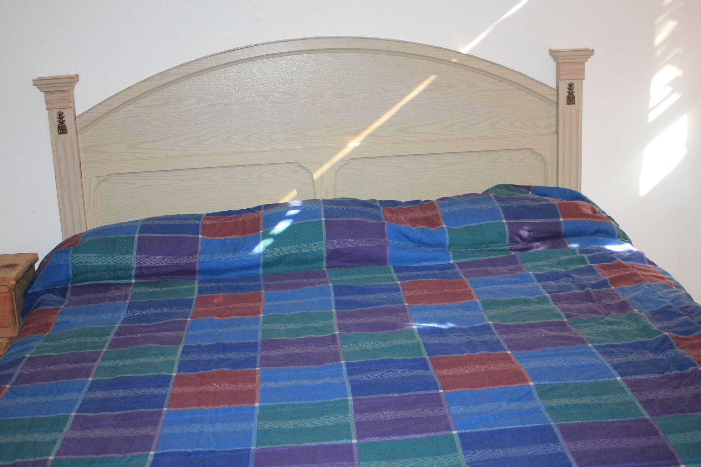 Una cama con cabecera de madera y colcha estampada de cuadros coloridos.