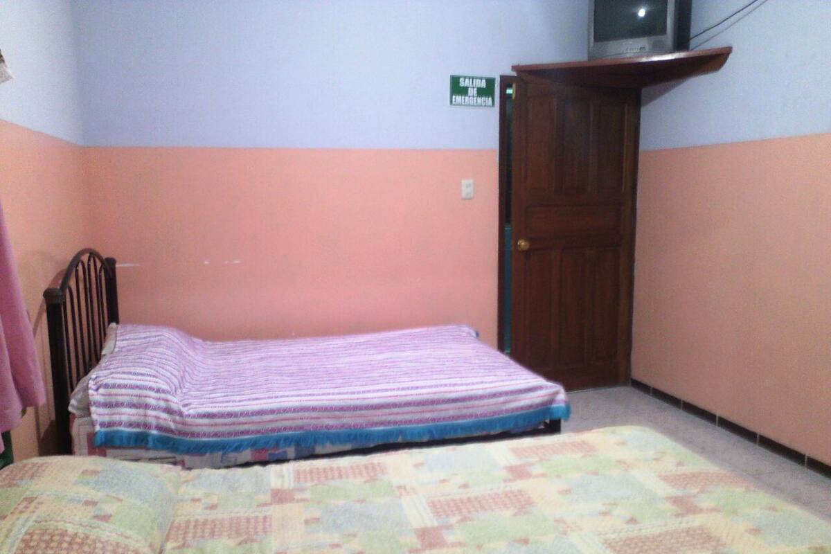 A bedroom with a bed, a wooden wardrobe, and a television on a stand.