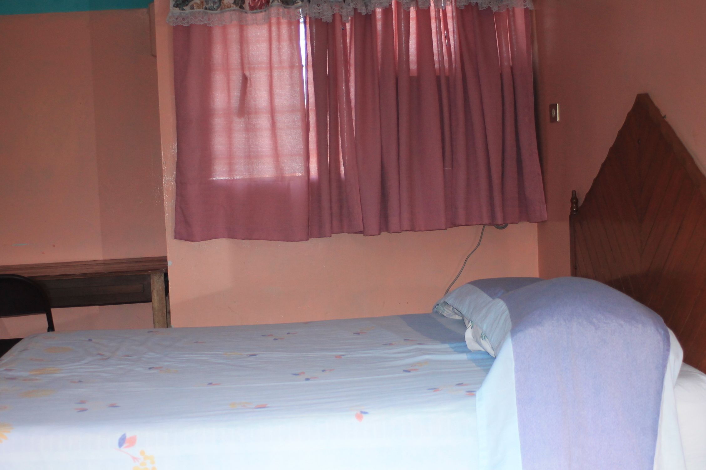Un dormitorio con una cama, cabecera de madera, una silla y una ventana con cortinas.