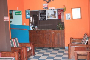 Un área de recepción con mostrador de madera, pared azul y naranja, y piso a cuadros.