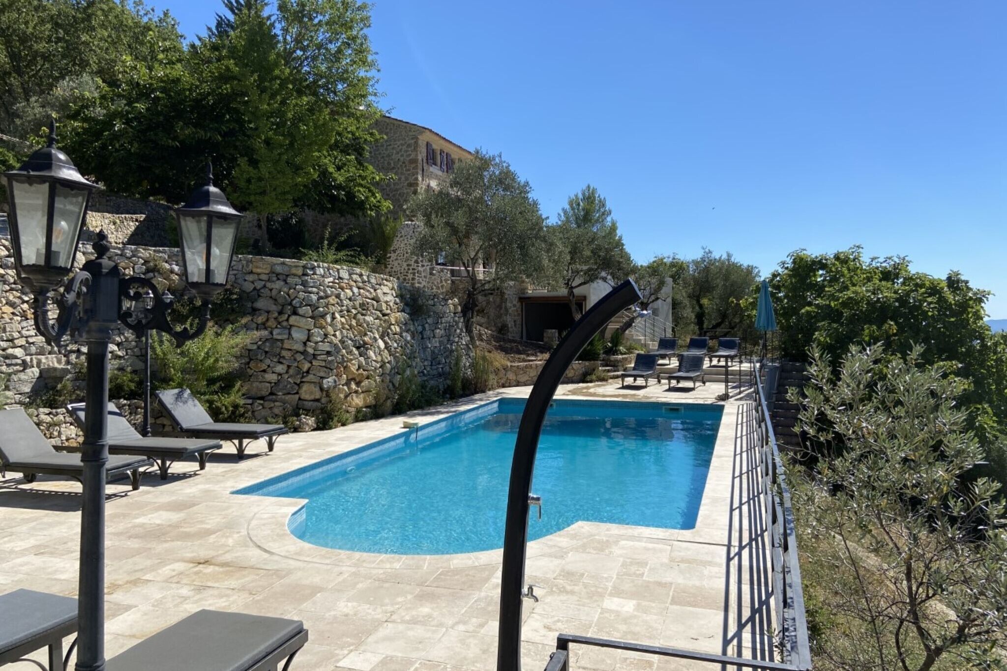 A rectangular swimming pool with a stone wall and lounge chairs.