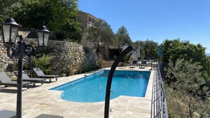 A rectangular swimming pool with a stone wall and lounge chairs.
