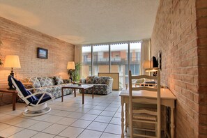 A living room with a brick wall, a sofa, a rocking chair, a table, and a chair. - Channel view 217 (Port Aransas)