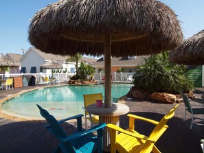 Relax by the pool surrounded by lush tropical plants and shaded seating areas.