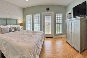 A bedroom with a large bed, a TV on a cabinet, and a door leading outside. - Sol Mates VW61 (Port Aransas)