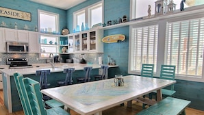 Une cuisine avec des meubles blancs, un grand îlot central et des chaises de couleur turquoise.