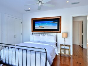 A bedroom with a bed, a ceiling fan, a framed picture on the wall, and a nightstand with a lamp. - Duval Penthouse (Key West)