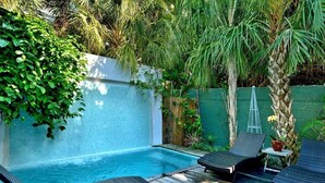 Ein privater Poolbereich mit Liegestühlen und einem kleinen Tisch, umgeben von üppiger Vegetation und einer weißen Mauer.