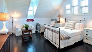 A bedroom with a sloped ceiling, a bed with white bedding, a nightstand, a lamp, a small table with a plant, and a sign that reads "BEACHES". - Bahamas House (Key West)