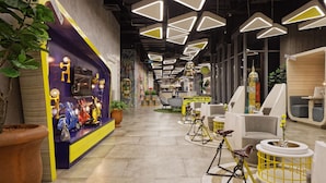 Un interior moderno con lámparas de techo geométricas, una zona de recepción con decoración colorida y un área de descanso con sillas originales.