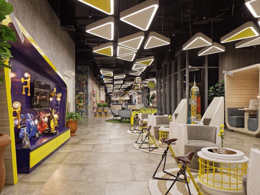 Un interior moderno con lámparas de techo geométricas, una zona de recepción con decoración colorida y un área de descanso con sillas originales.