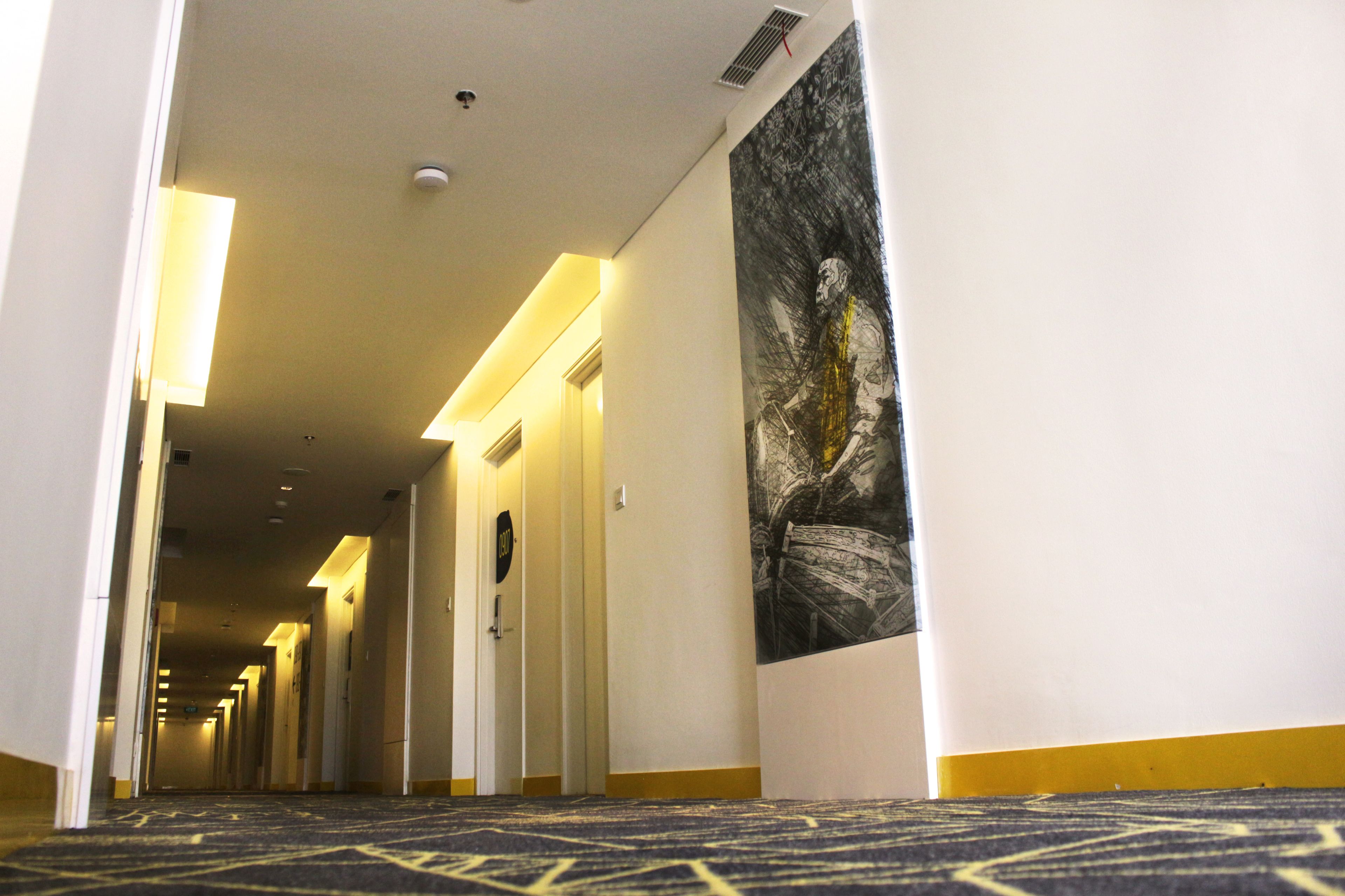 A hotel hallway with a patterned carpet, doors, and a large black and white poster on the wall.