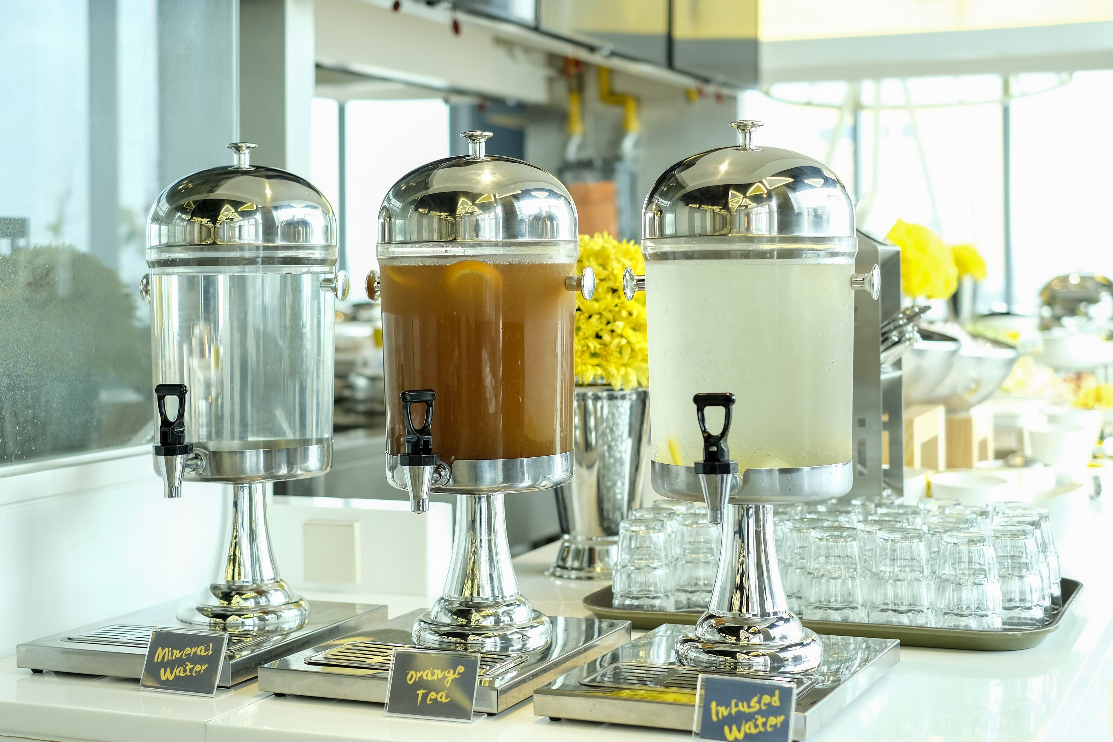 Eine Getränkestation mit drei Spendern, beschriftet mit 'Mineralwasser', 'Orangetee' und 'Infused Water'.