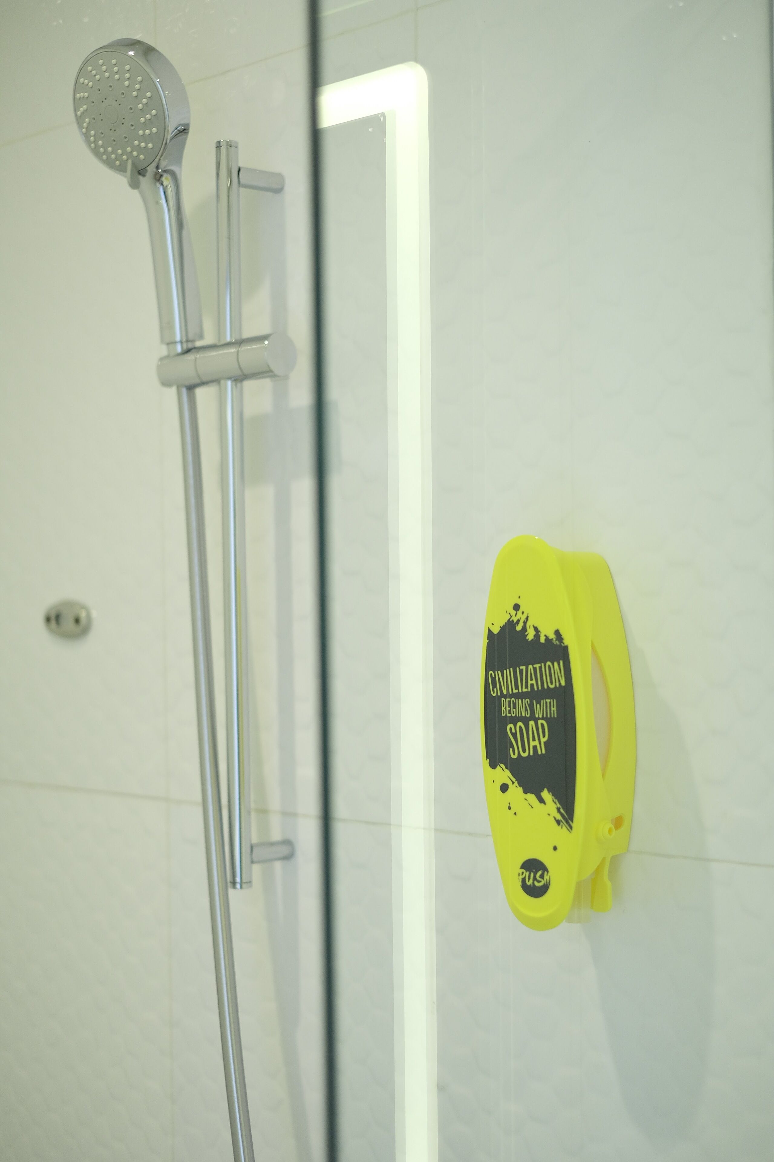 A shower with a handheld showerhead and a yellow soap dispenser on the wall.