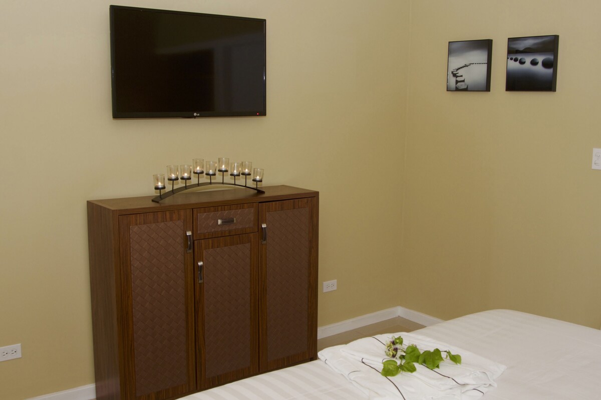 Une chambre à coucher comprenant un lit, une commode en bois, un téléviseur à écran plat et deux tableaux encadrés accrochés au mur.